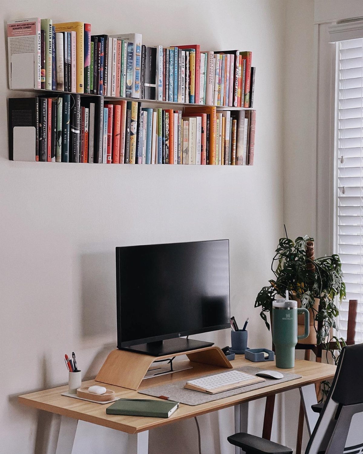 Light wood desk with a monitor and long floating bookshelves filled with books.
