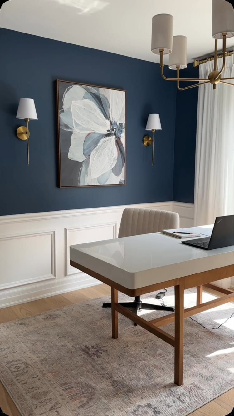 Modern home office with navy blue walls, white wainscoting, and a minimalist desk.
