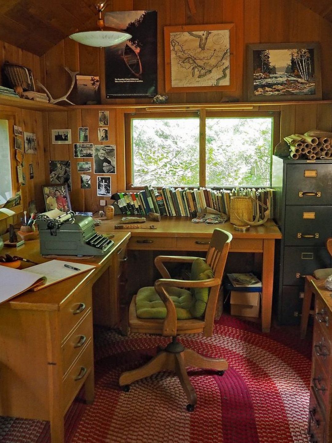Wooden home office with vintage typewriter, wood-paneled walls, and red patterned rug.