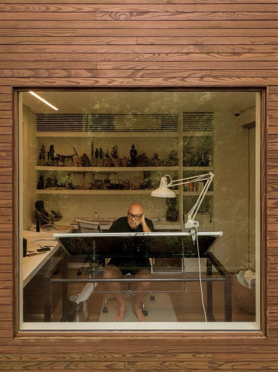 Man sitting at a modern desk in a wood-paneled studio with figurine shelves.