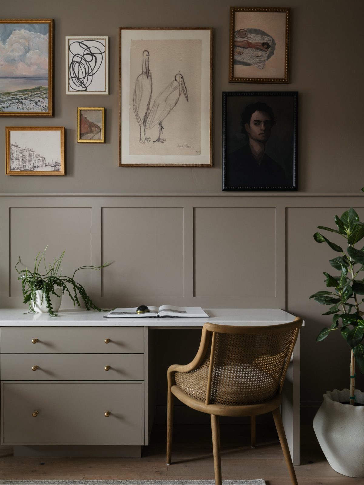 Grey home office desk with a woven chair and gallery wall of art.