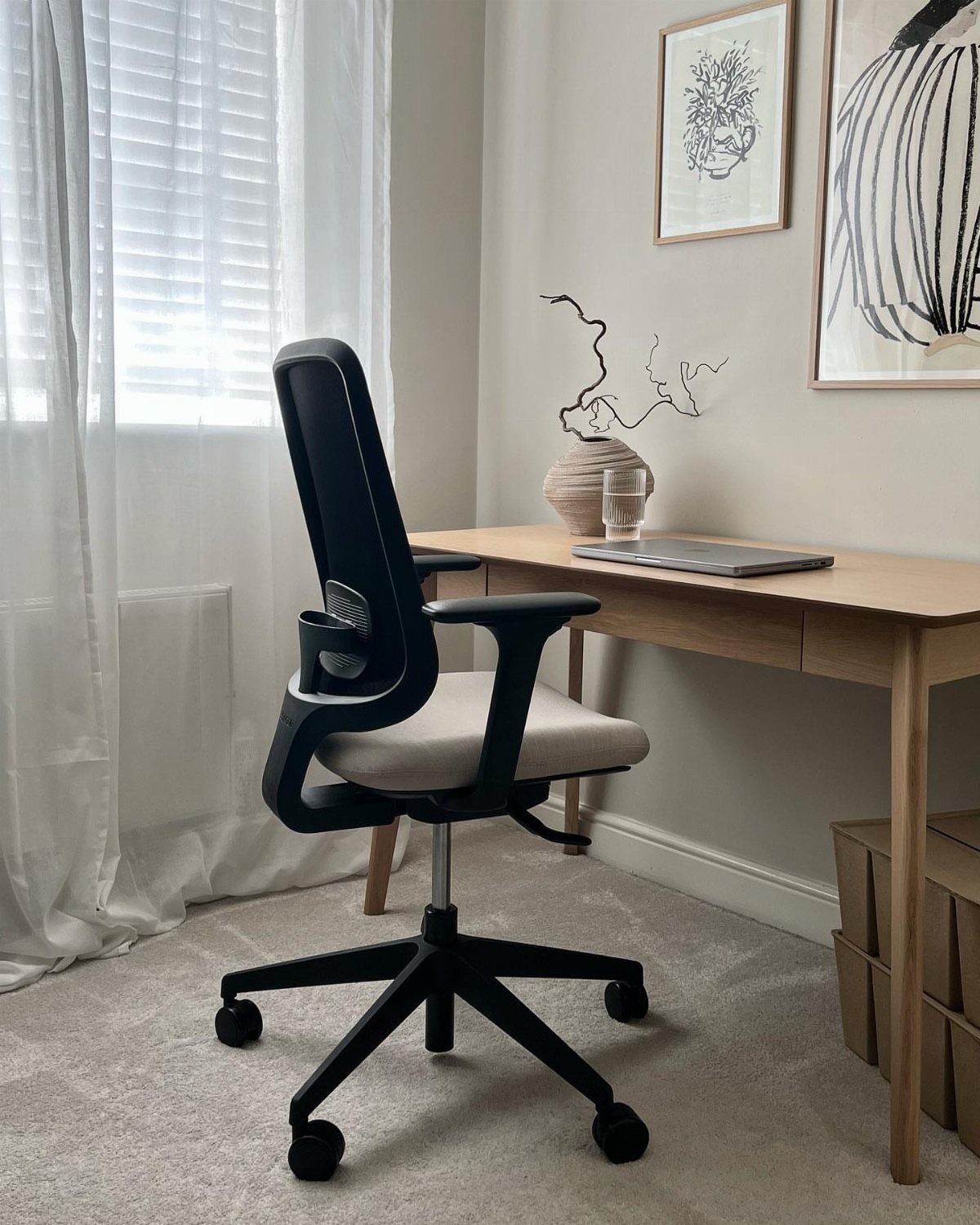 Black ergonomic task chair next to a light wood desk in a bright room.