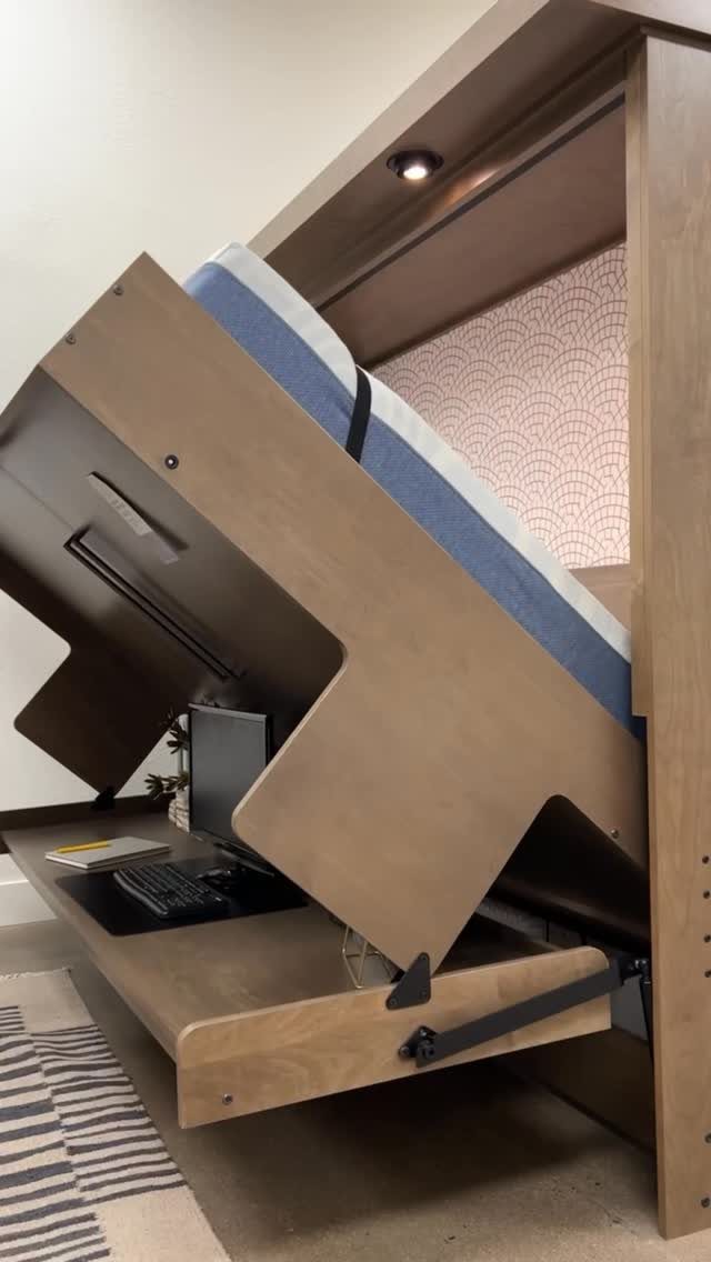 Wooden wall bed partially lowered to reveal a compact desk with a computer monitor.