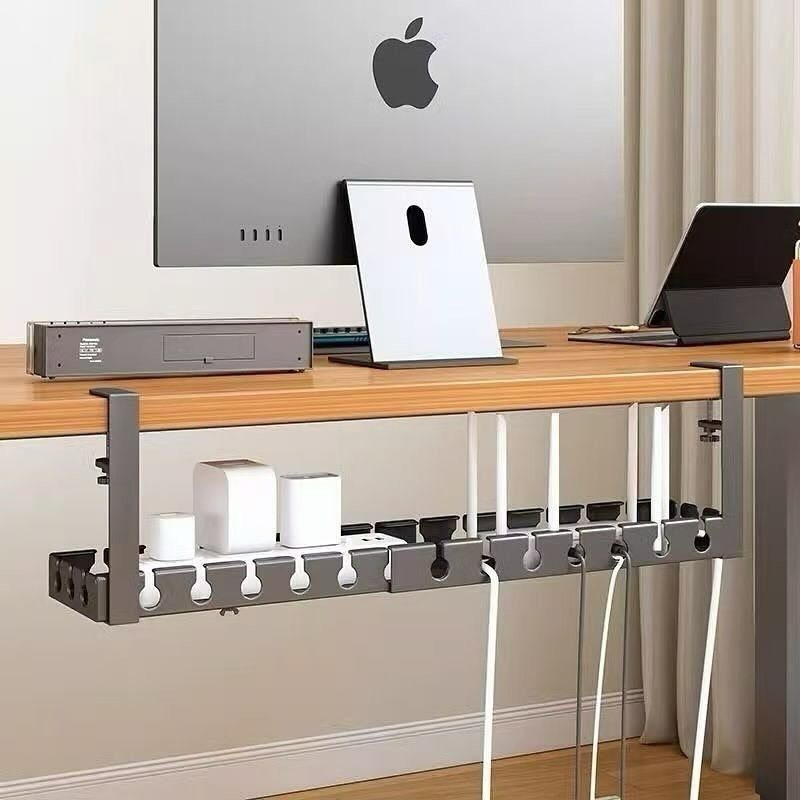 Grey cable management tray under a wooden desk organizing white power cords and adapters