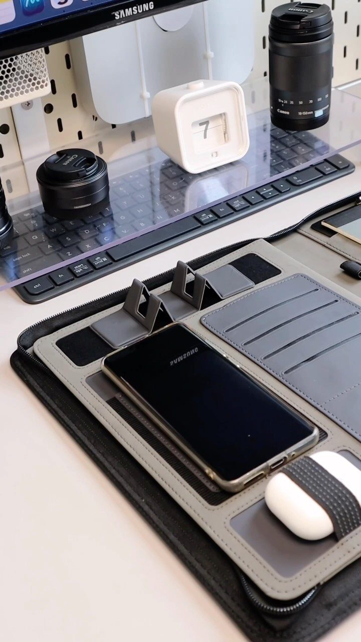 Desk setup with a smartphone, keyboard, camera lens, and Samsung monitor on white surface.