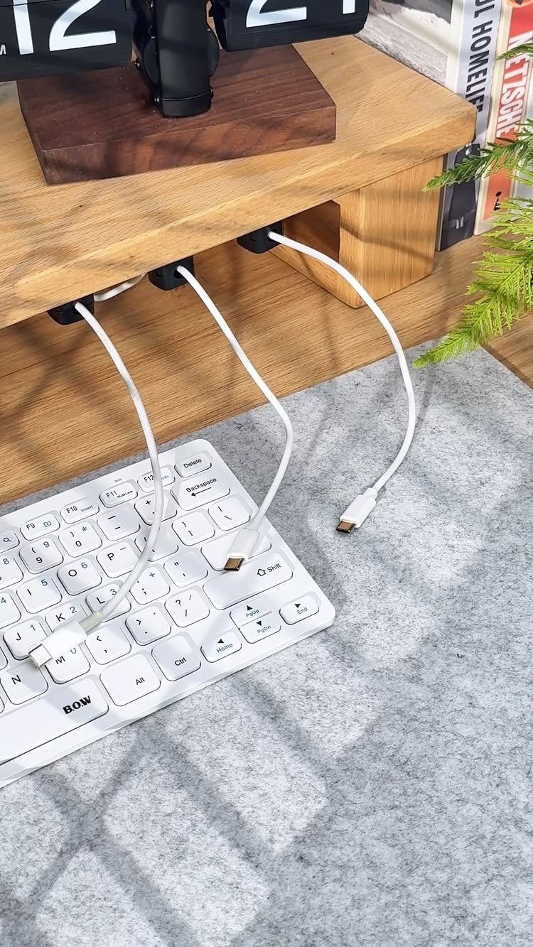 Black cable clips holding white wires under a wooden desk above a keyboard