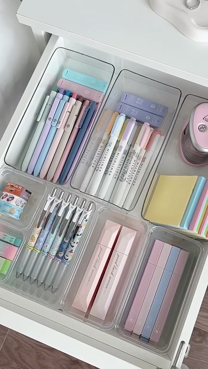 Clear plastic desk organizers in a white drawer filled with colorful stationery.