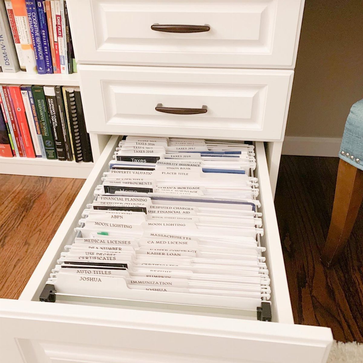 White filing cabinet drawer open to show organized hanging folders with labeled tabs.
