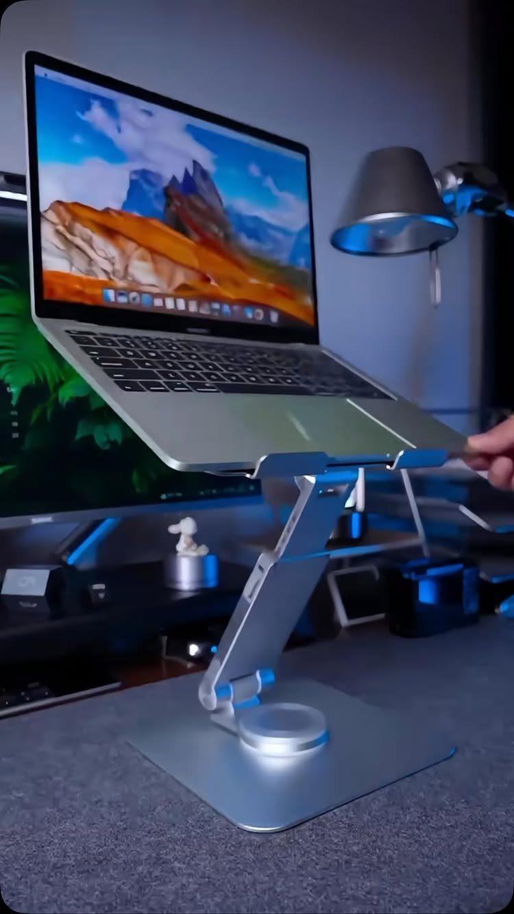Silver laptop on an adjustable metal stand on a grey desk with blue lighting