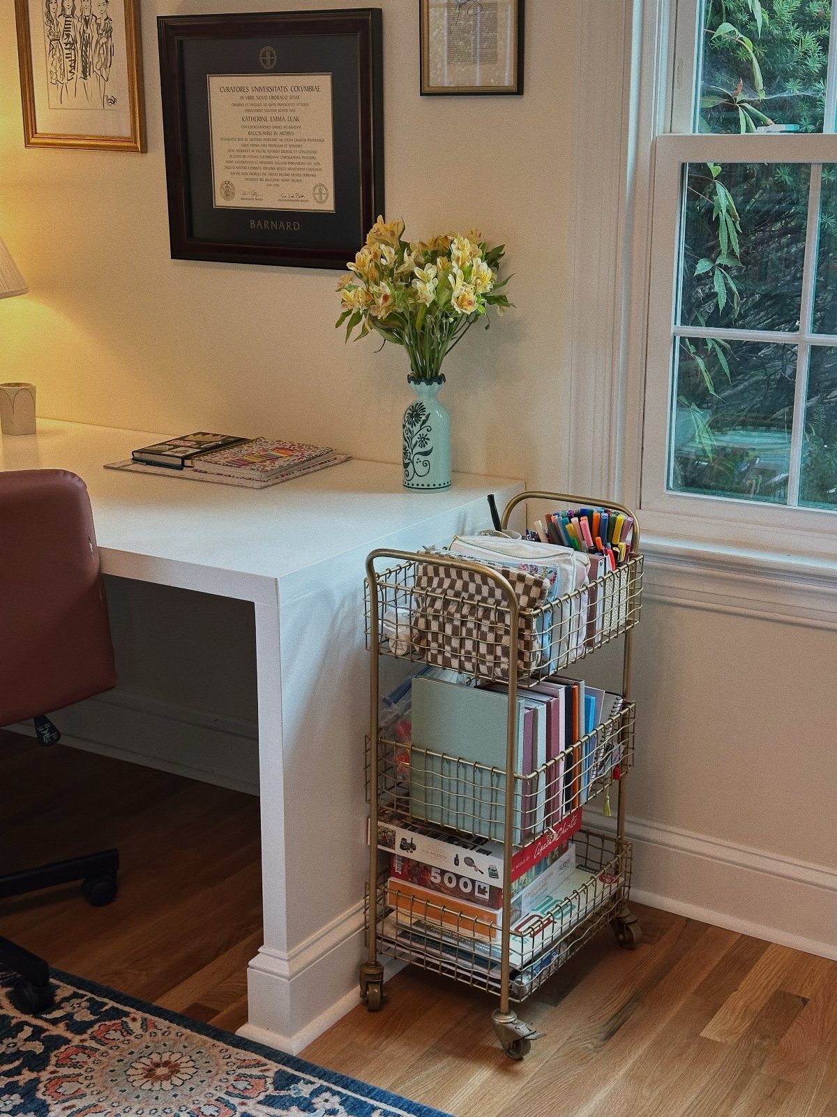 White home office desk with a gold rolling utility cart and yellow flowers.