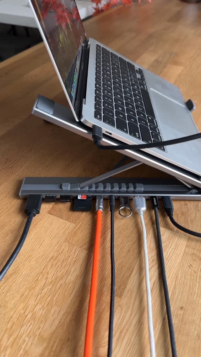 Laptop on a metal stand connected to a multi-port docking station on wooden desk
