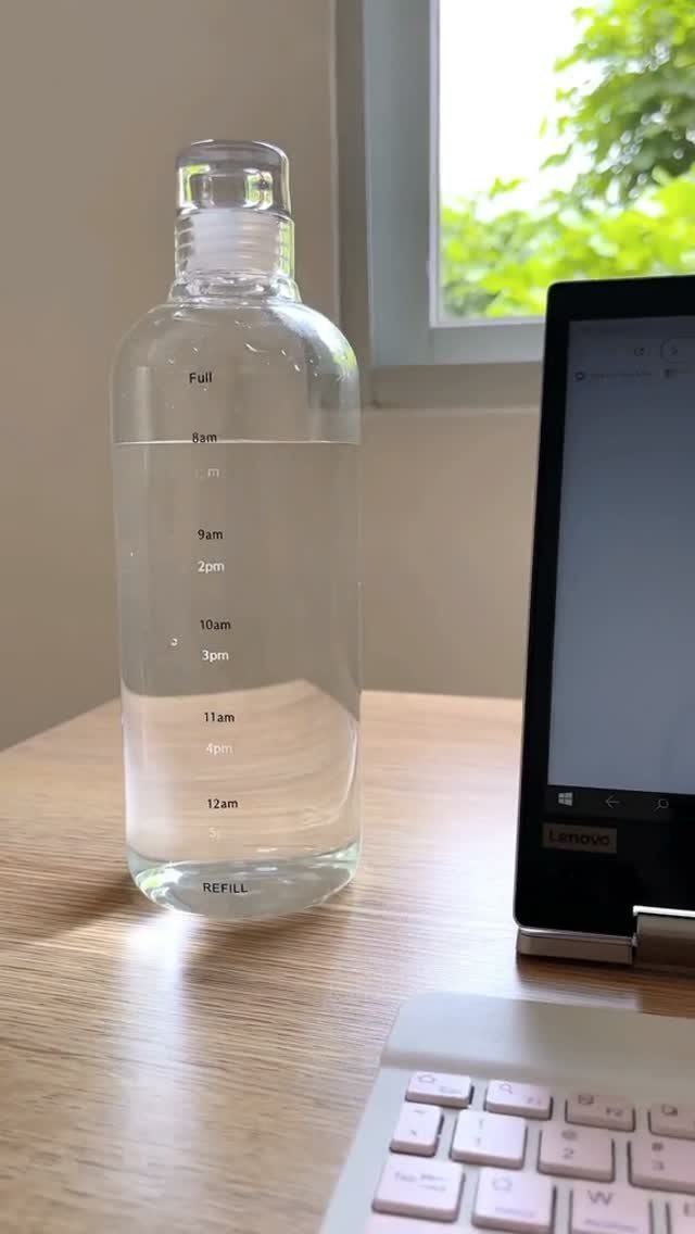 Clear water bottle with time markers on a wooden desk next to a laptop