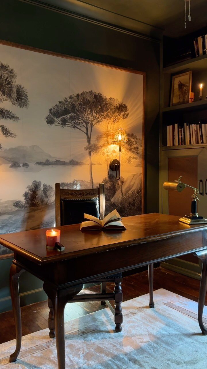 Dark green home office walls with a wooden desk and landscape mural.
