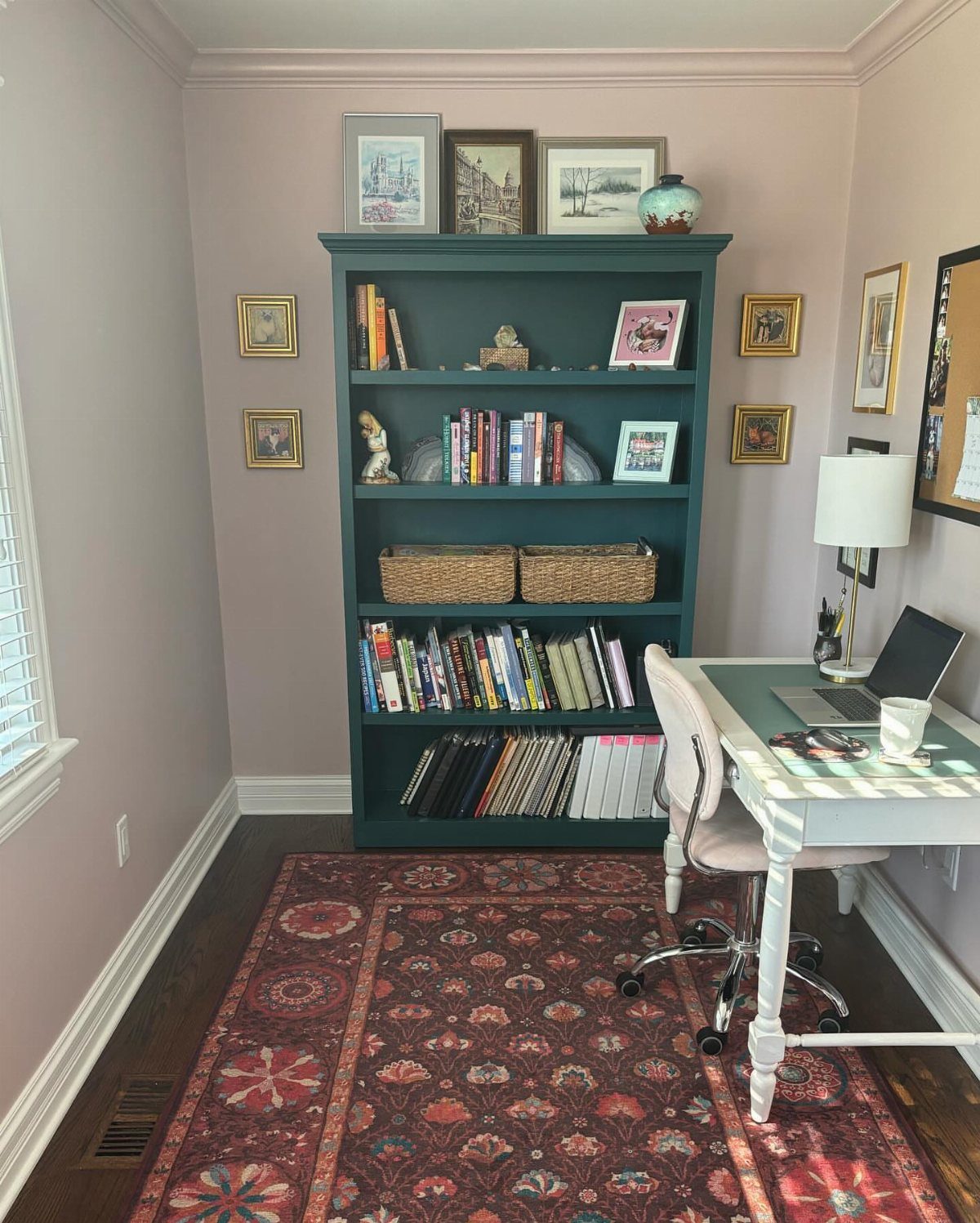 Mauve walls and a dark teal bookshelf in a home office setting.