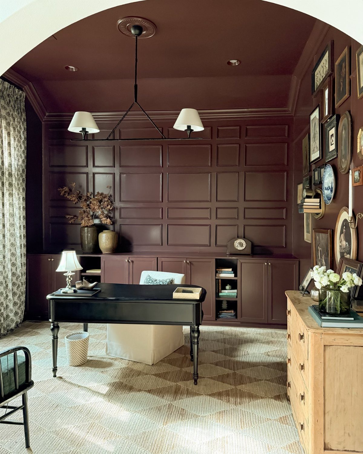 Deep red home office with paneled walls, black desk, and gallery wall art.
