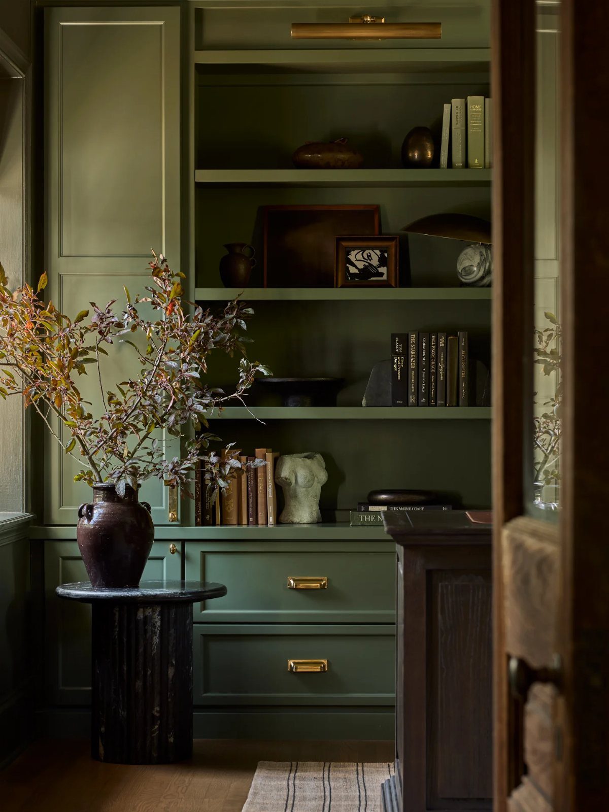 Olive green built-in bookshelves and walls in a home office with decorative accents.