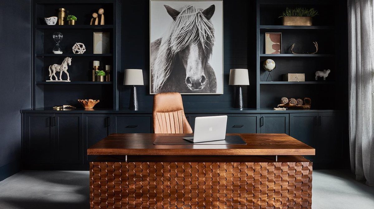 Dark navy blue home office with wooden desk and horse portrait on wall