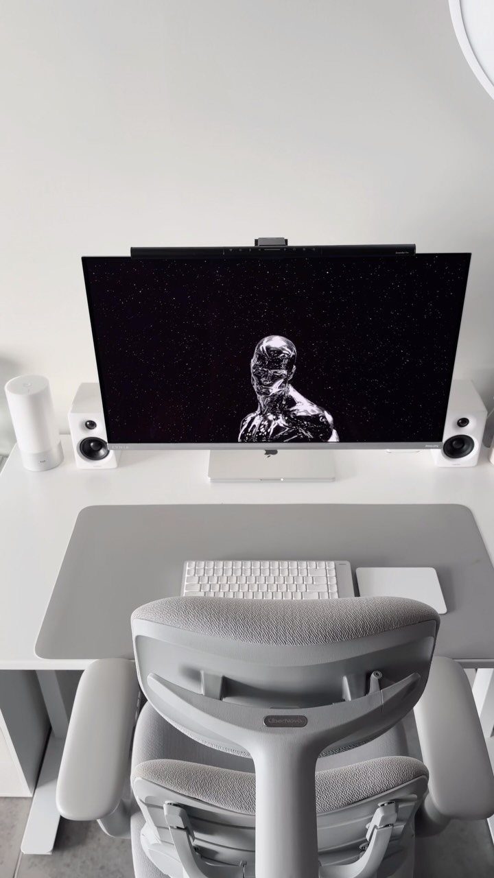 Minimalist home office with white desk, monitor, and gray ergonomic chair against white walls