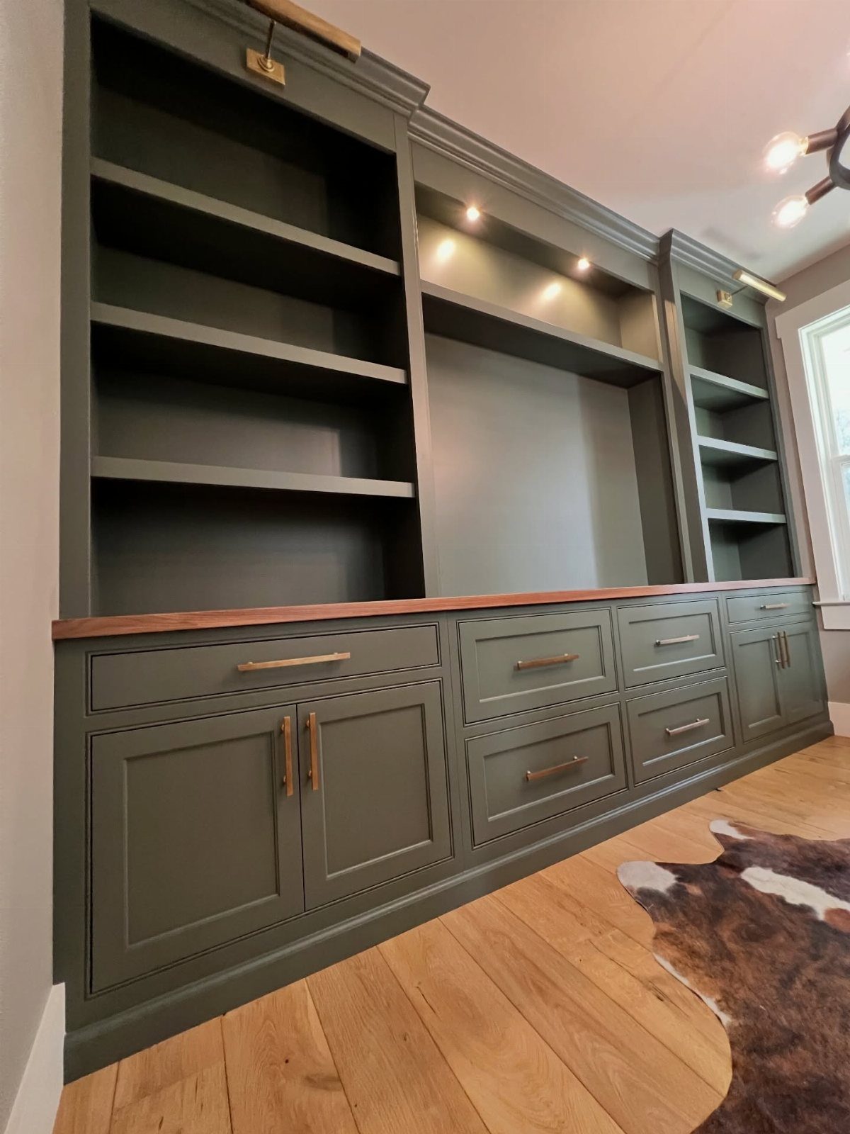 Dark green built-in shelving and cabinets with a wooden countertop and light wood flooring.