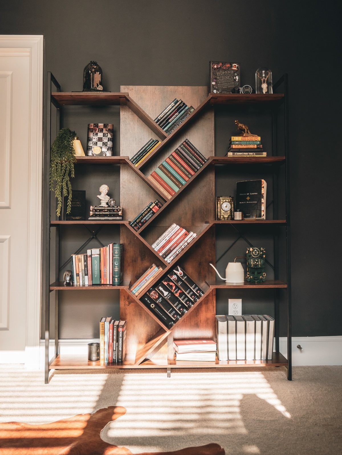 Freestanding wooden bookshelf with diagonal central shelves and black metal frame against dark wall