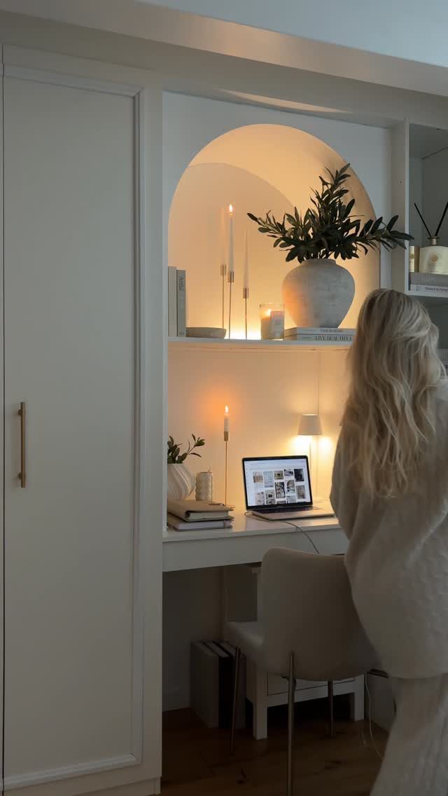 Woman standing at a white built-in desk with a laptop and warm lighting.