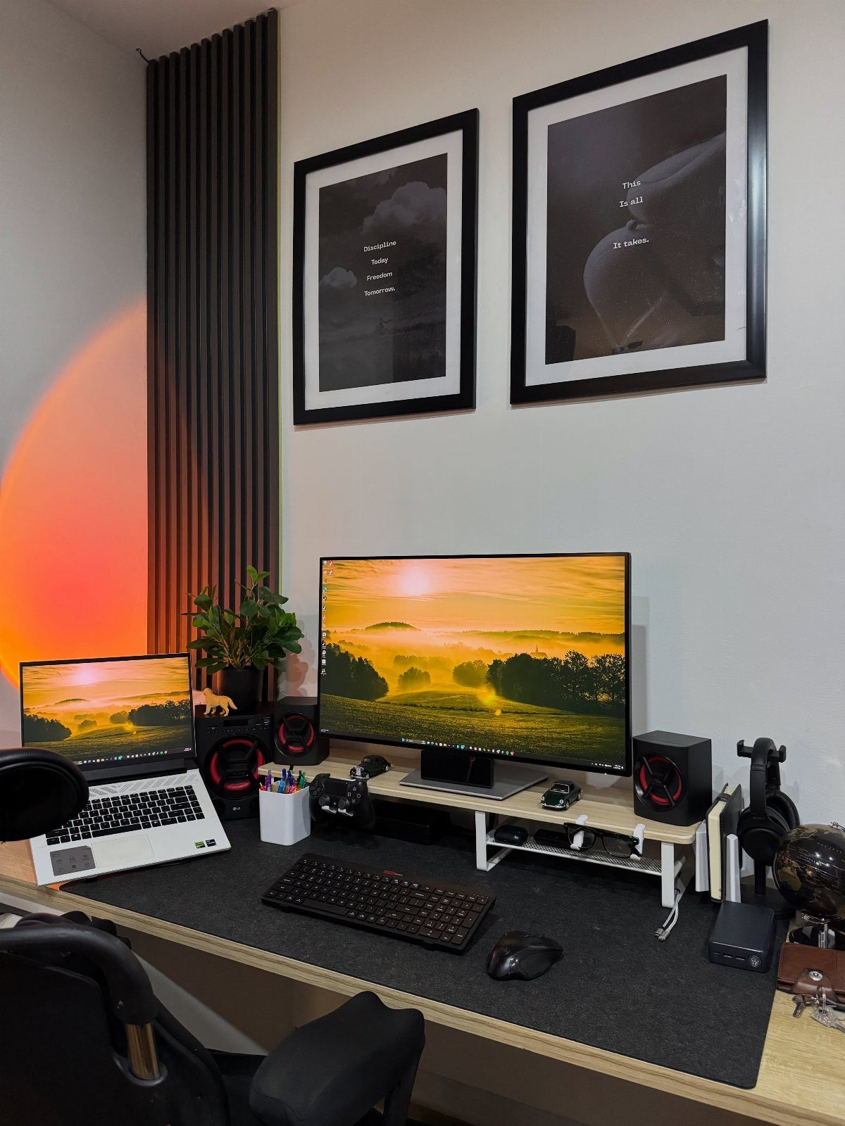 Home office desk with dual screens, a laptop, and framed wall art.