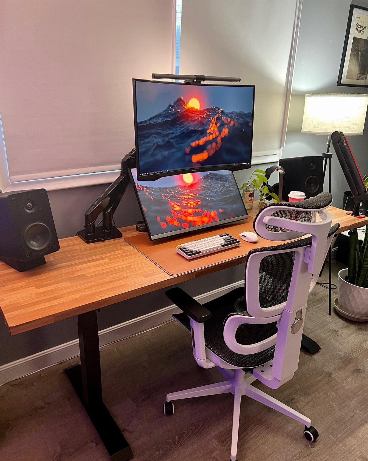 Ergonomic white mesh chair and adjustable standing desk with dual monitors and speakers.
