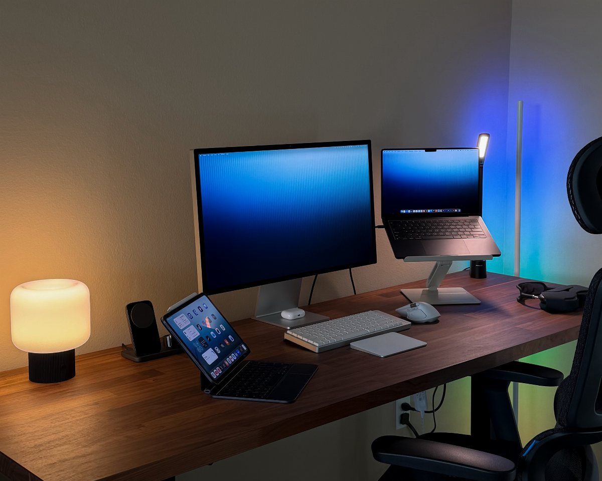 Wooden desk with a monitor, laptop, tablet, and lamp in a home office.