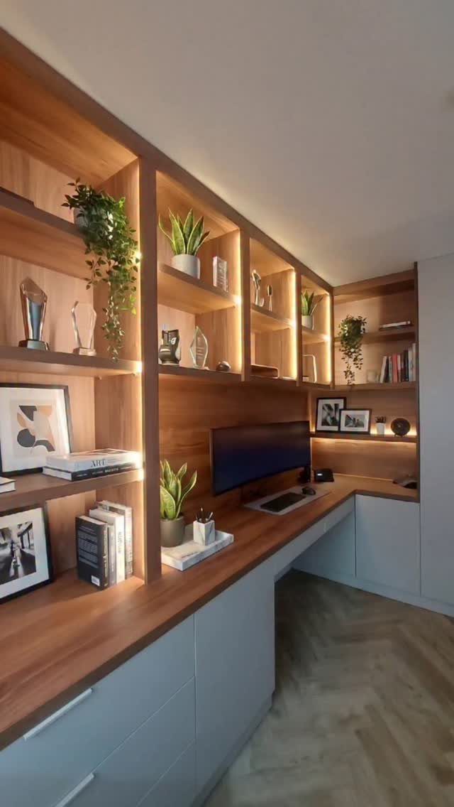Modern home office desk with integrated warm LED lighting in wooden wall shelves.