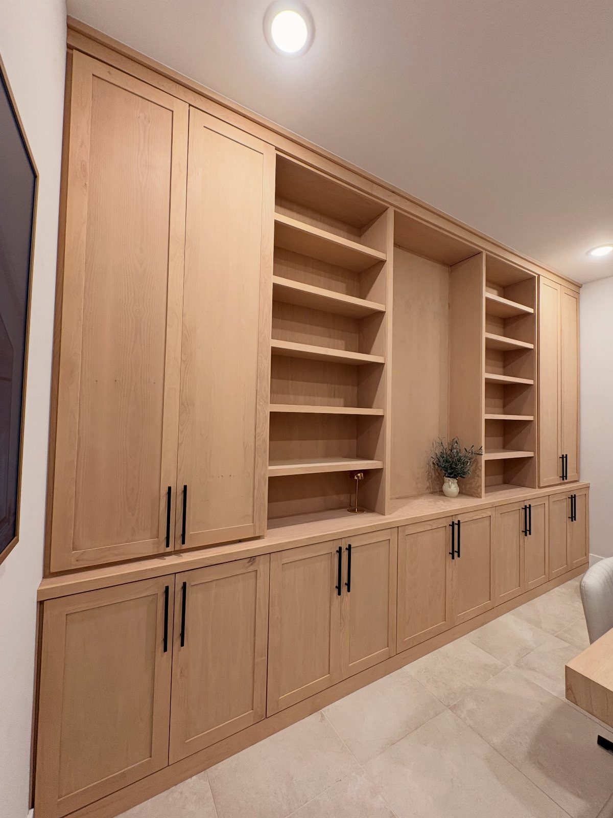 Light wood built-in wall unit with open shelves and closed storage cabinets.