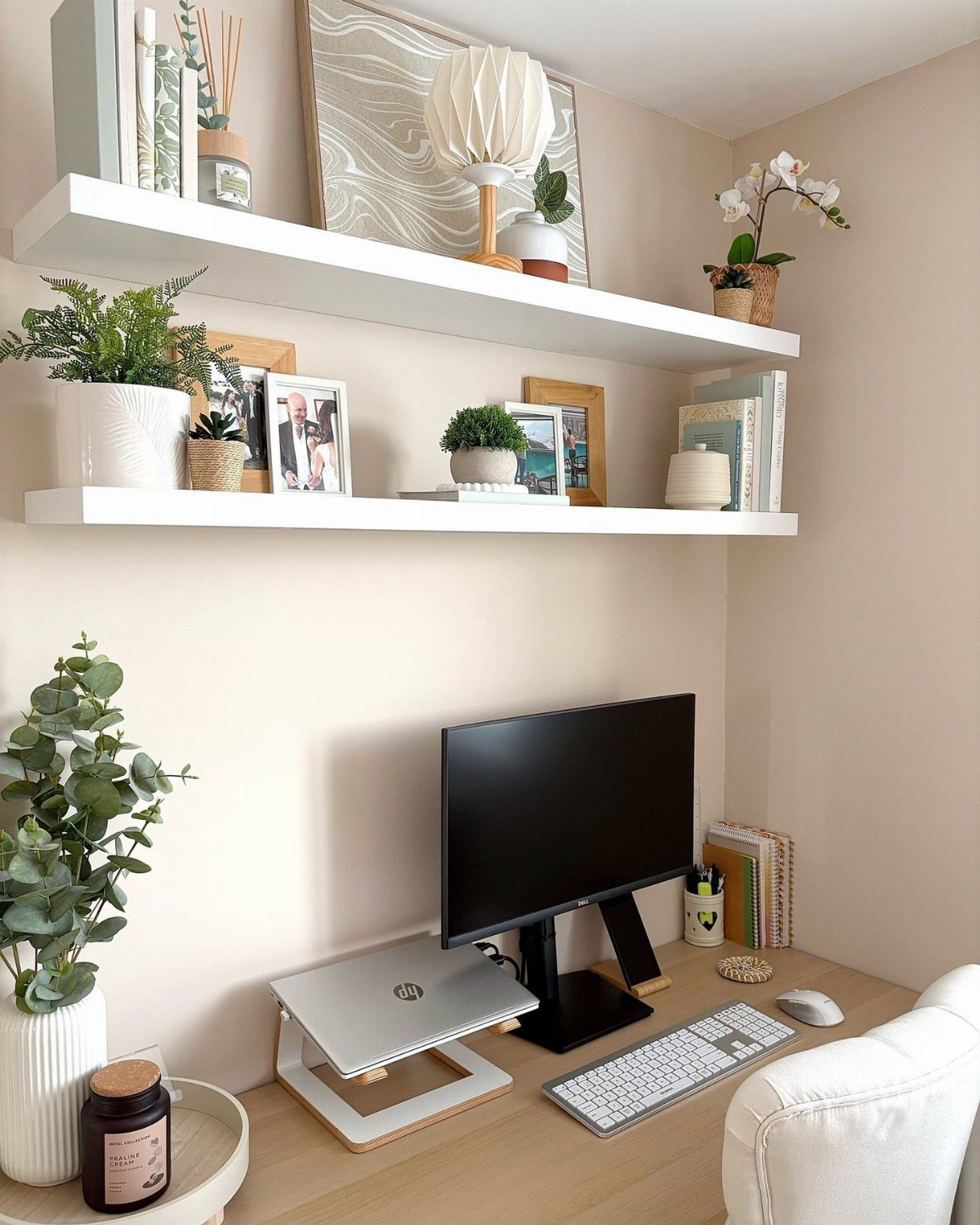 Home office desk with monitor and laptop under white shelves with decor and plants