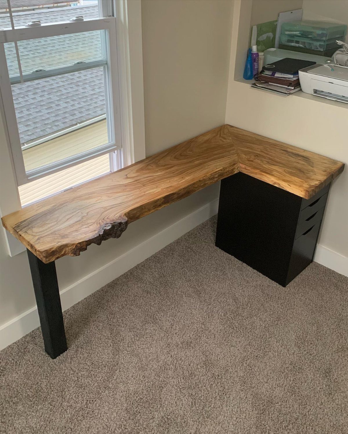 Live edge wooden corner desk with black drawers next to a window
