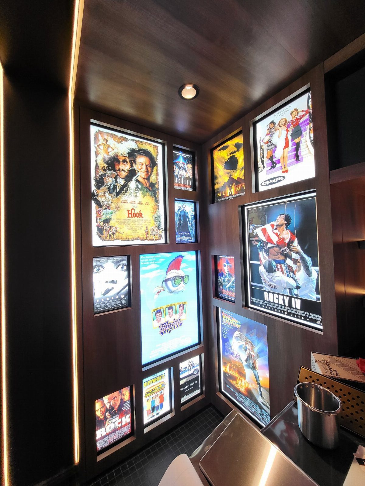 Backlit movie posters displayed on dark wood walls in a home theater room.