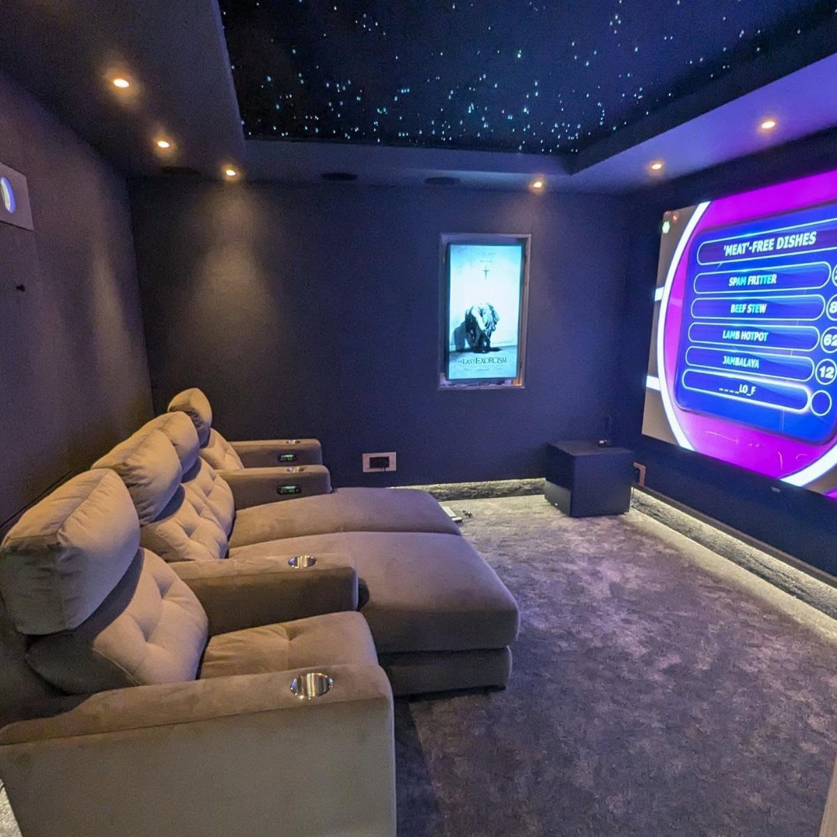 Grey oversized reclining theater seats with cup holders in a dark basement cinema.