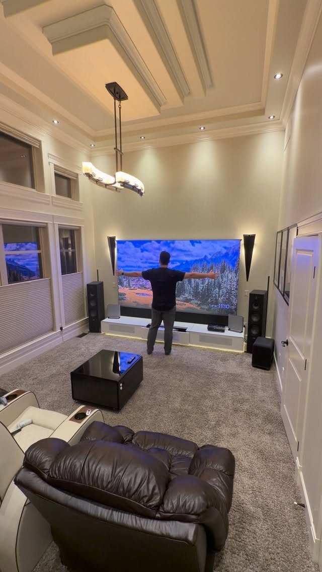 Modern home theater room with large screen, leather recliners, and tray ceiling lighting.
