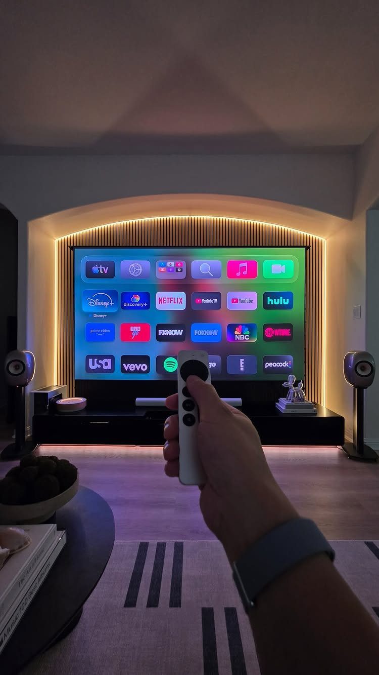 Hand holding a remote pointing at a large TV in a modern home theater