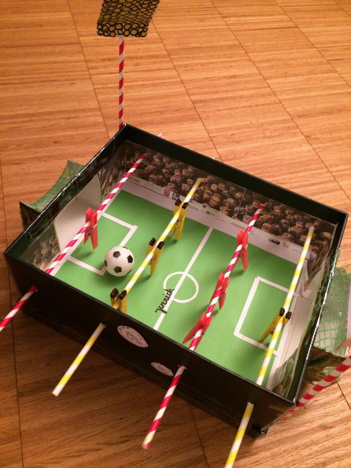 Homemade table football game made from a cardboard box and striped straws.