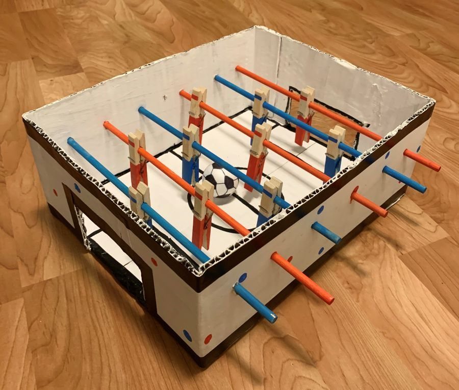 Homemade table football game made from cardboard and colored rods on wooden floor