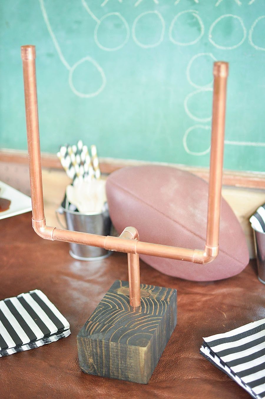Copper pipe goalpost on a wooden base with an American football behind it.