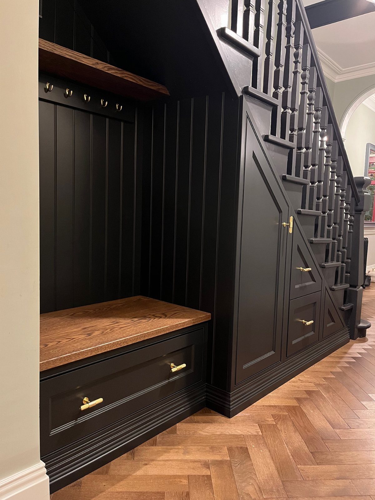 Black built-in hall tree with wooden bench and drawers under a staircase.