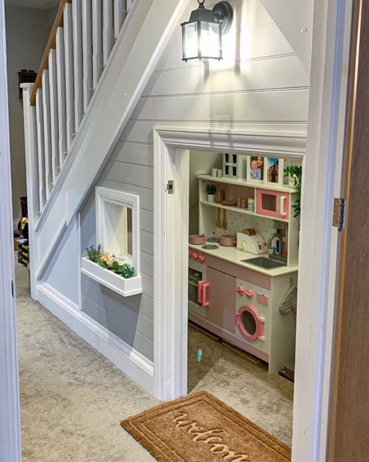 Children's play kitchen built into a cozy nook under a grey staircase.
