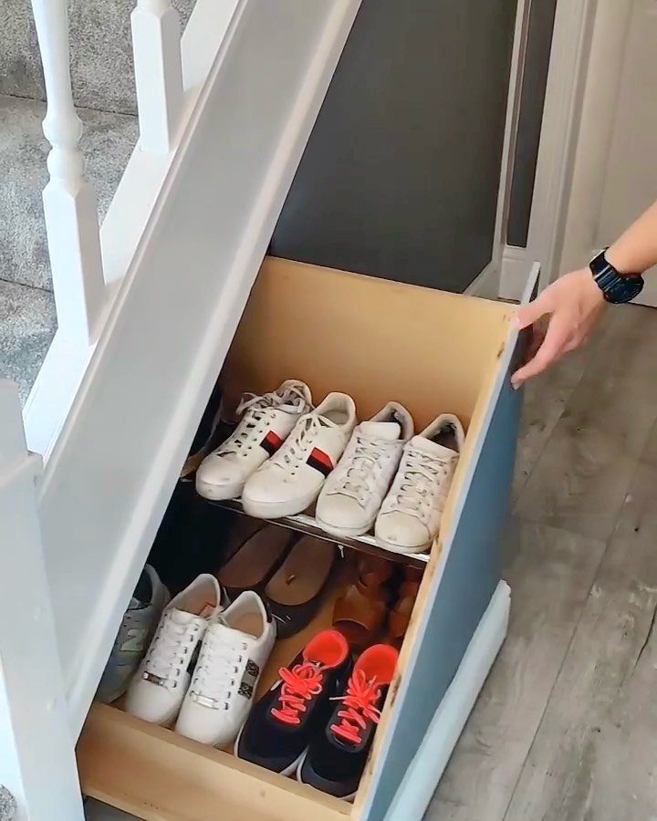 Pullout wooden drawer under white stairs filled with organized sneakers and shoes.