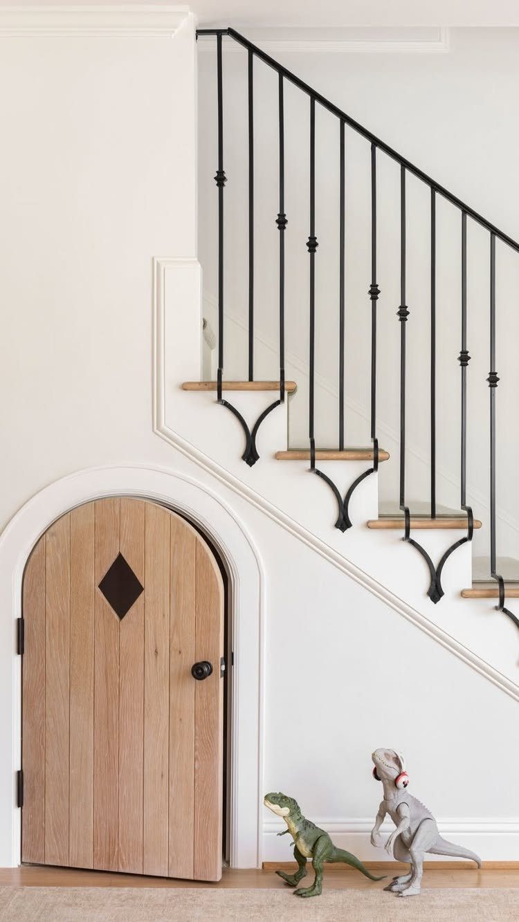Arched wooden door built under a white staircase with black metal railings.