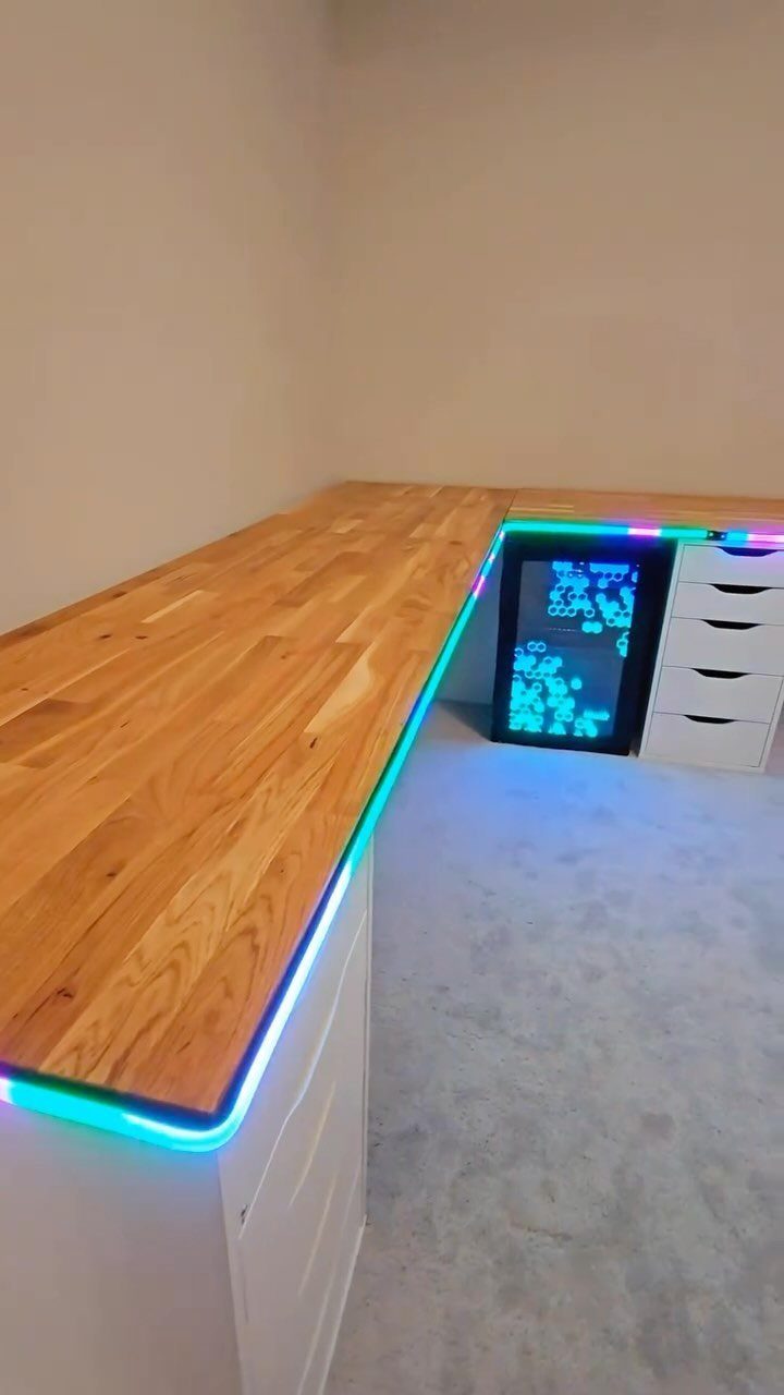 L-shaped wooden desk with white Alex drawers and cyan LED under-glow lighting.