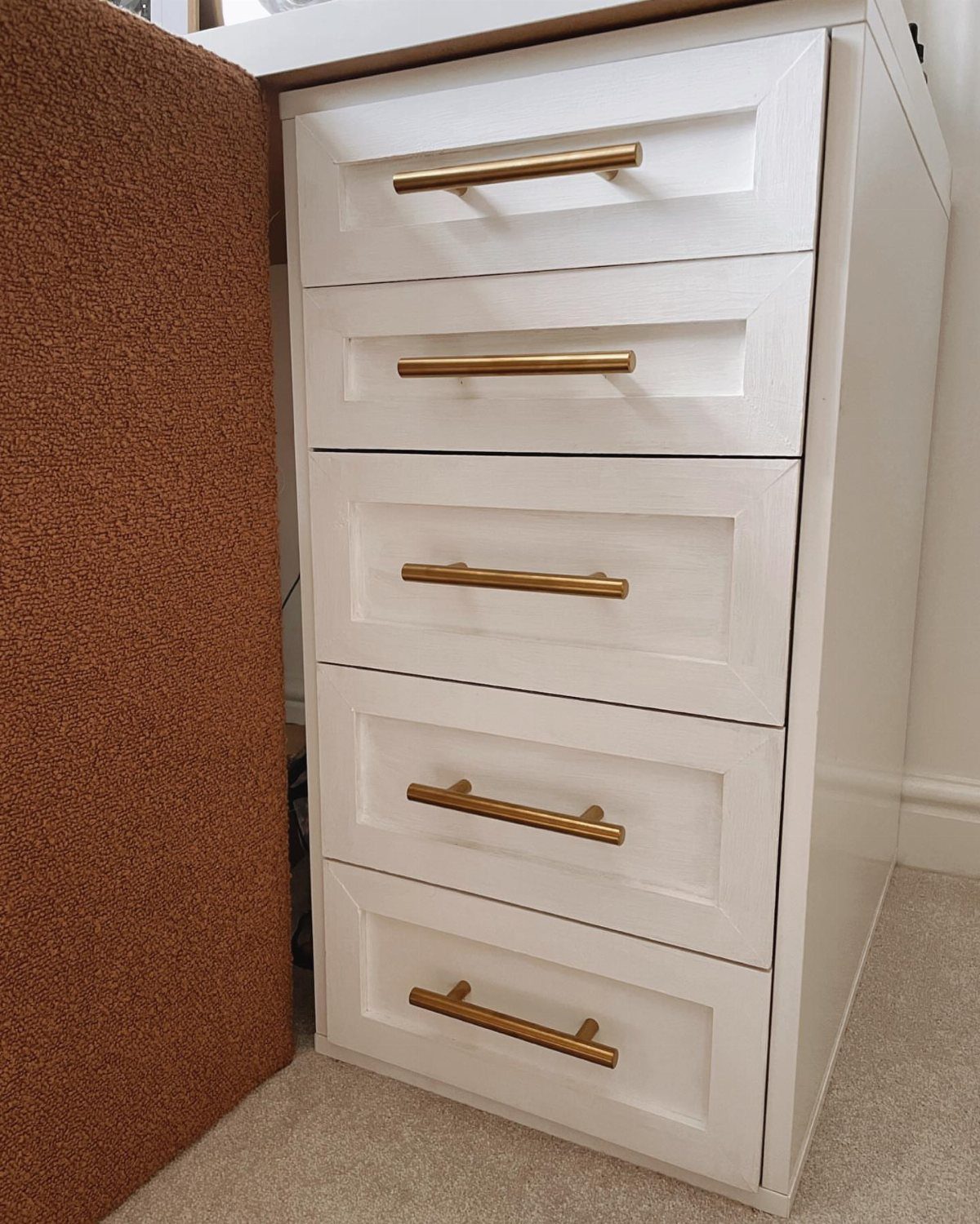 White IKEA ALEX drawer unit with shaker-style fronts and gold handles next to corkboard