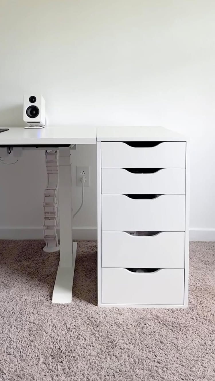 White desk with an adjustable standing leg and a white five-drawer storage unit.