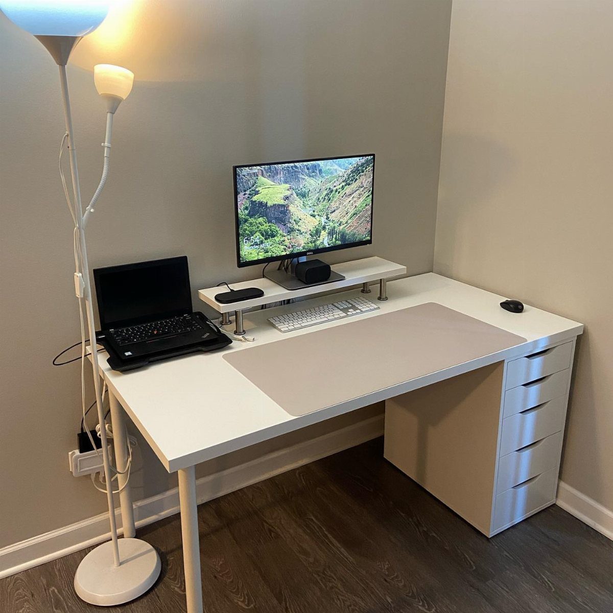 White modern desk with computer monitor, laptop, and white drawer unit in office.