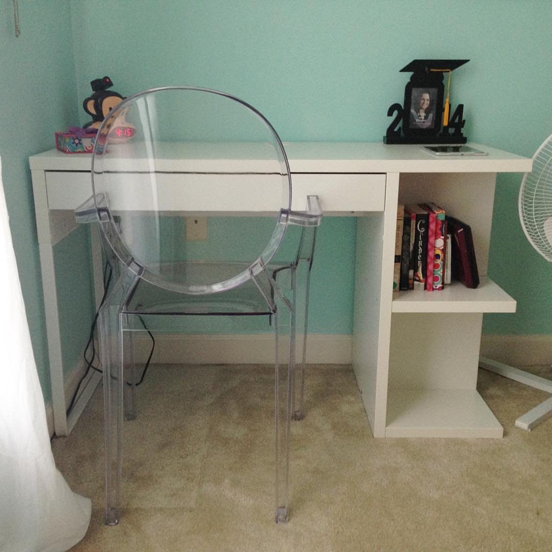 White desk with side shelving and a clear acrylic chair against blue wall