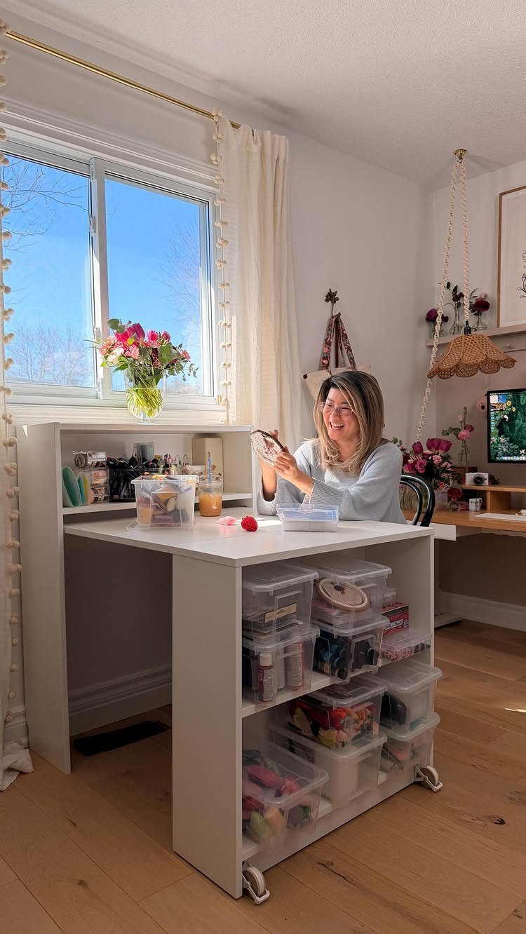 Woman sitting at a white mobile desk with storage bins in a bright room.