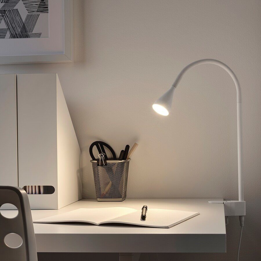 White LED desk lamp illuminating a notebook and stationery on a white desk.